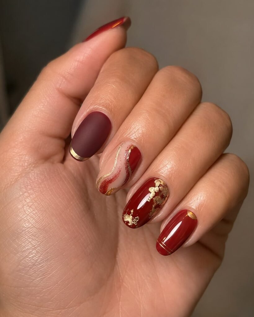 Mixed red and gold manicure with French tips, swirls, foil-style accents, and fine metallic lines.