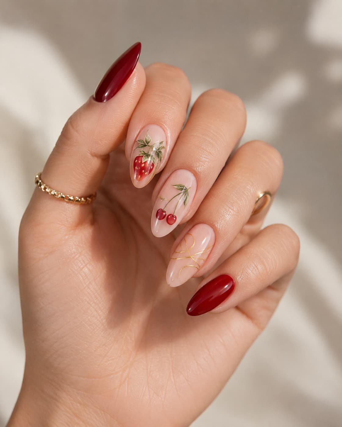 Almond nails with strawberry, cherry, deep red, nude, and gold details
