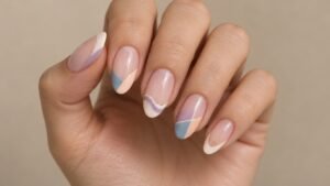Adult hand with nude nails featuring curved, wavy, geometric, and negative-space French tips.